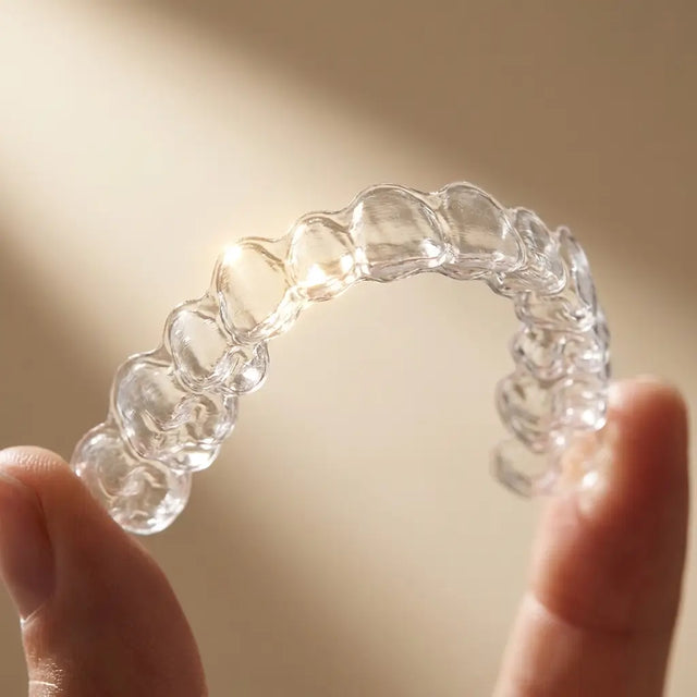 Crystal-clear aligner catching the light, held in fingers