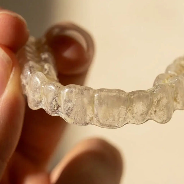 Close-up of a cloudy, film-covered clear aligner held in fingers.